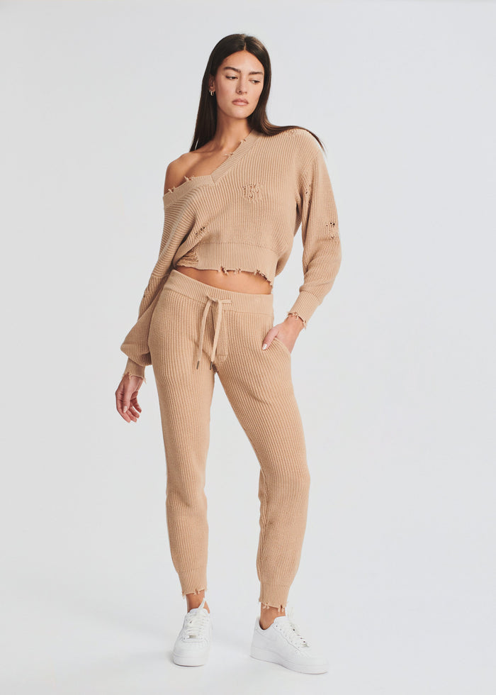 Angled front view of a model in a beige Ida Jogger knit set with a one shoulder cropped sweater and joggers. media 4 of 4