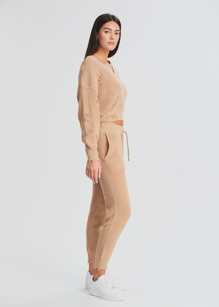 Side view of a woman wearing a beige Ida Jogger knit set with a cropped sweater and drawstring joggers, white sneakers. media 2 of 4