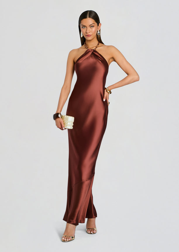 Anat Dress in bronze satin halter gown with a twisted neckline full length model holding a cream clutch
