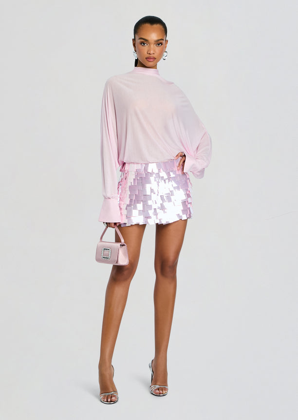 Model wearing Bennedetta Sequin Skirt ensemble with a soft pink draped top, pastel pink sequin mini skirt, and matching handbag.