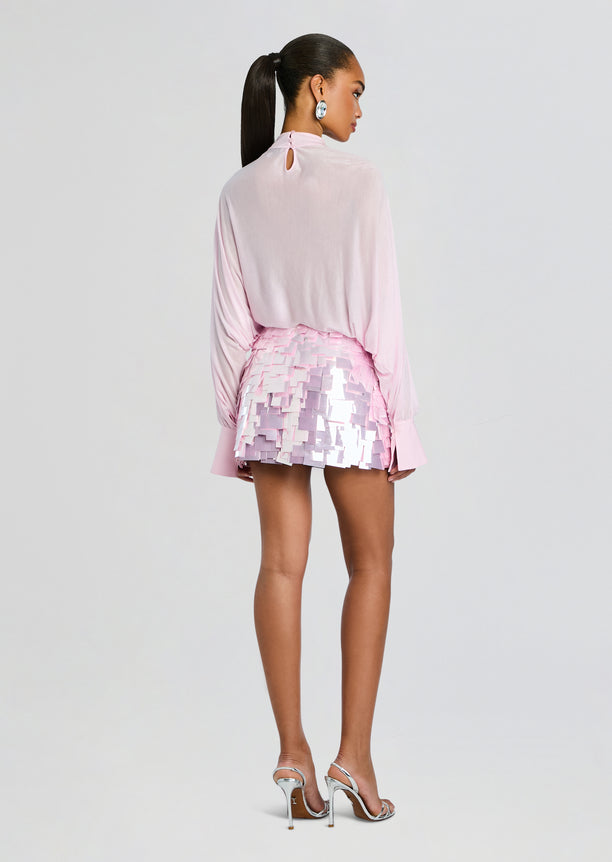 Back view of a model in a pale pink blouse and a pink sequin patchwork mini skirt.
