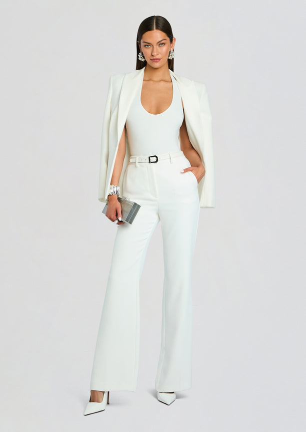 Model in pale mint Eira Pant suit with blazer draped over shoulders, white top, belt and pointed white heels.