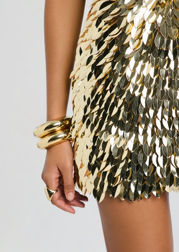 Close up of the Kariella Embellished Dress fabric showing gold and silver leaf sequins and a stack of gold bracelets on the model’s wrist.