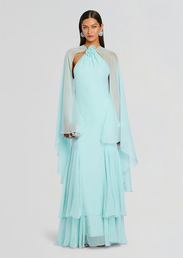 Full-length view of a model in a pale blue Lirael Chiffon Dress with a draped cape and layered hem.