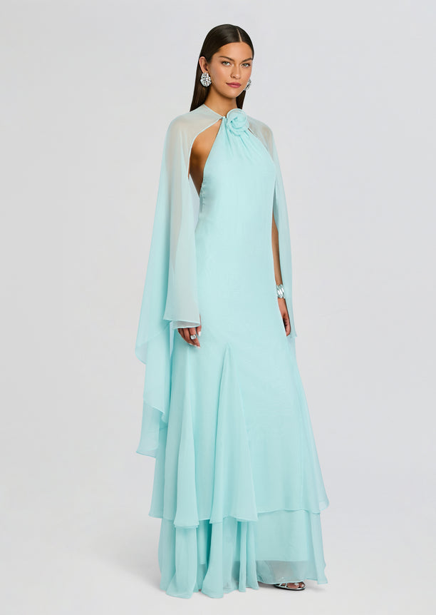 Model in Lirael Chiffon Dress in pale aqua with sheer cape overlay and pleated floor-length skirt