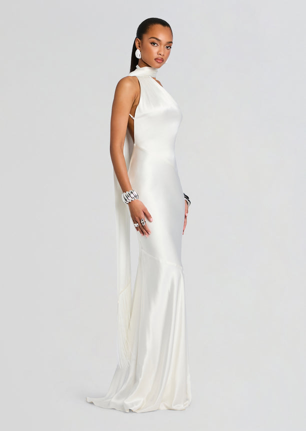 Kelsa Dress on a model in ivory satin halter neck with open back and tasseled fringe at the hem