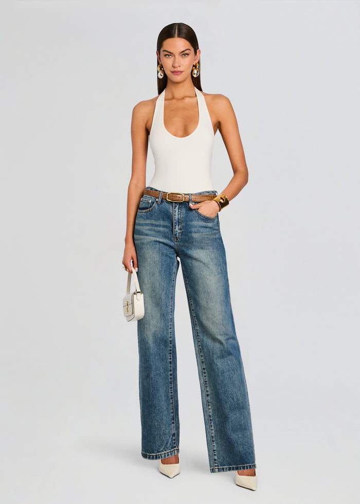 Model wearing white bamboo halter bodysuit with blue wide-leg jeans and a tan belt, carrying a small white bag. media 2 of 5