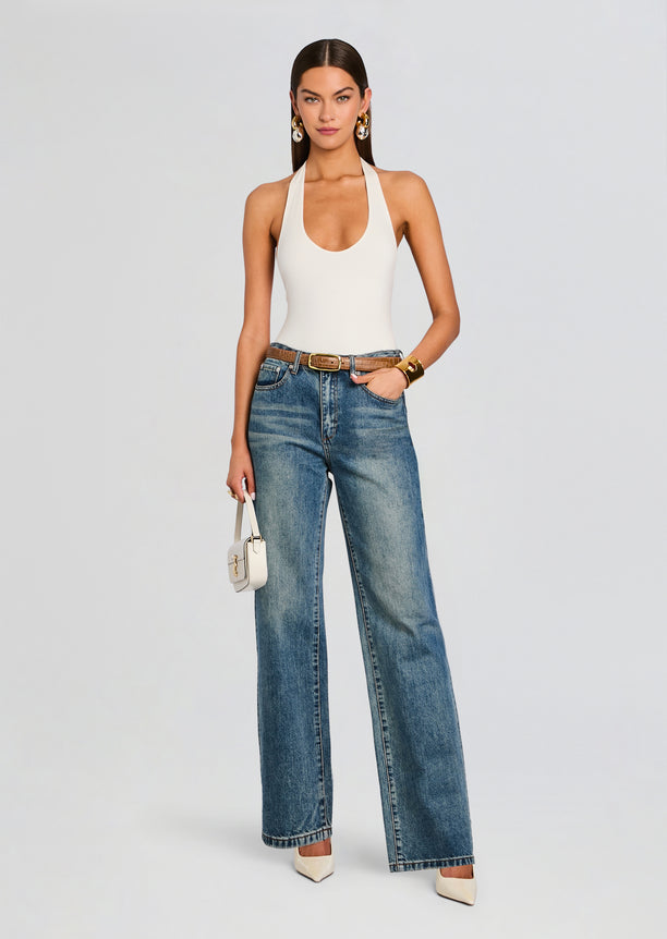 Model wearing white bamboo halter bodysuit with blue wide-leg jeans and a tan belt, carrying a small white bag.