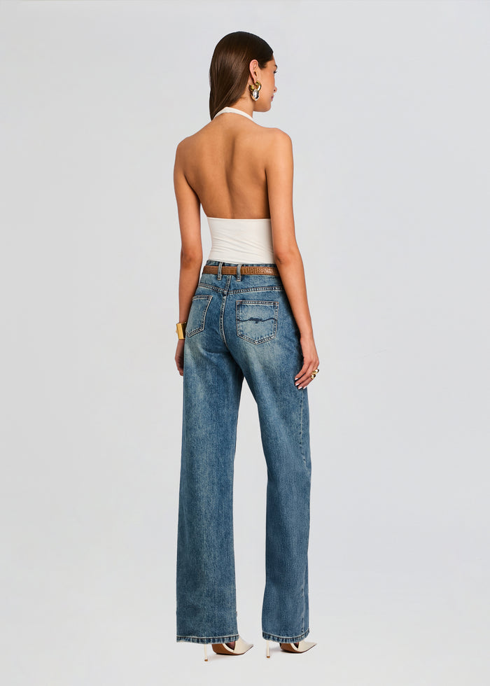 Back view of a model wearing a white bamboo halter bodysuit with high-waisted blue jeans. media 5 of 5