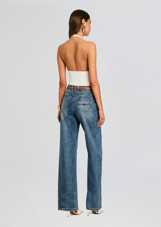 Back view of a model wearing a white bamboo halter bodysuit with high-waisted blue jeans.