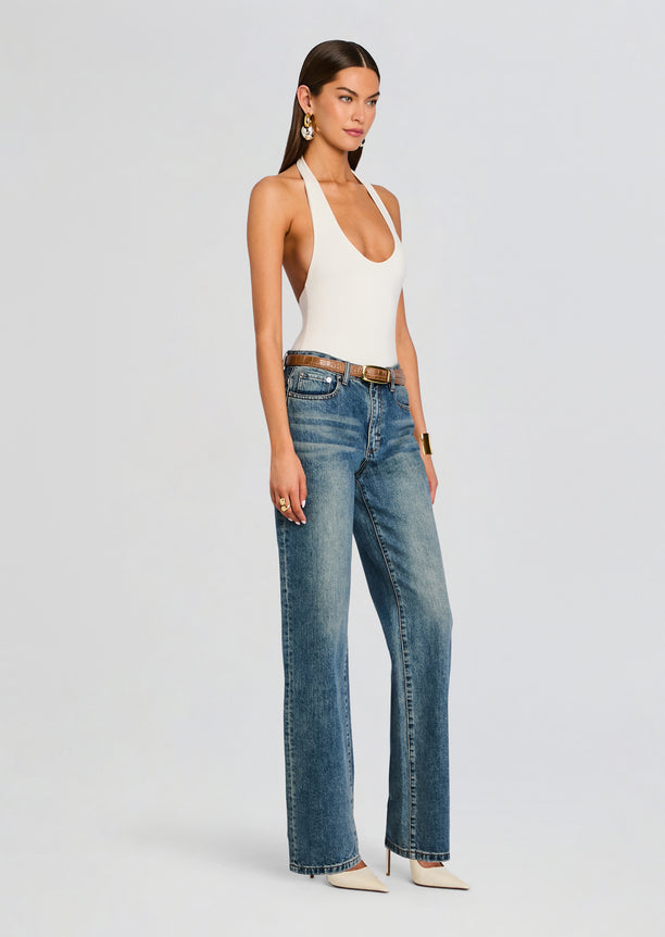 Model in a white bamboo halter bodysuit with high waisted jeans and gold accessories