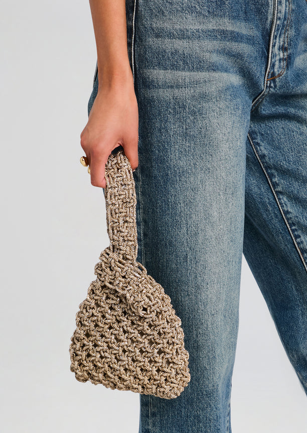 Niky Bag in beige beaded crochet style held by a hand against blue denim jeans