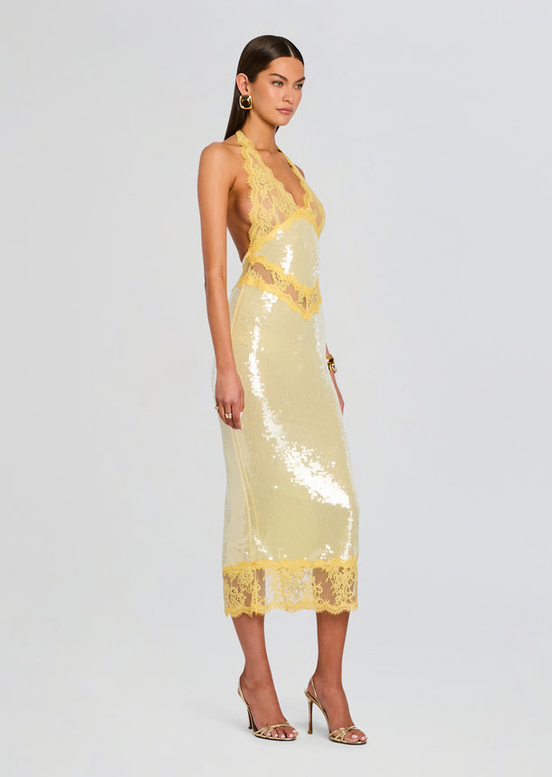 Side view of model in Vicky Sequin Lace Dress showing yellow lace halter and gold sequin midi silhouette with lace hem.