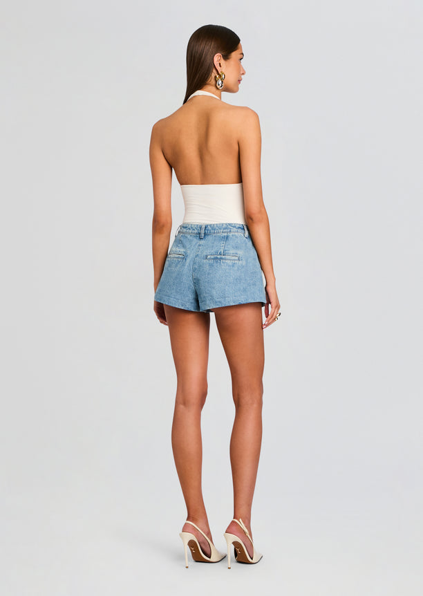 Back view of a model wearing light wash denim shorts and a white halter top.