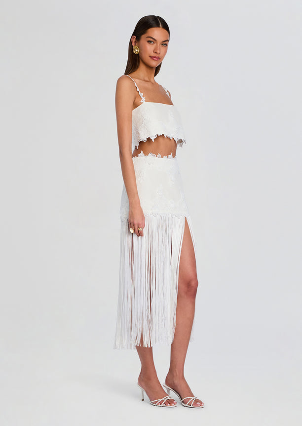 White lace crop top with delicate floral trim paired with a long fringe skirt on a model