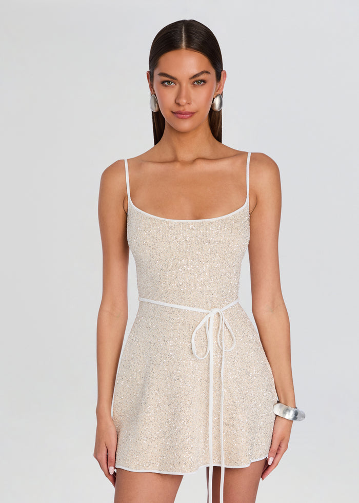 Gisele Dress on a model wearing champagne sequin mini dress with thin straps and a white belt, styled with silver earrings and bracelet. media 5 of 5