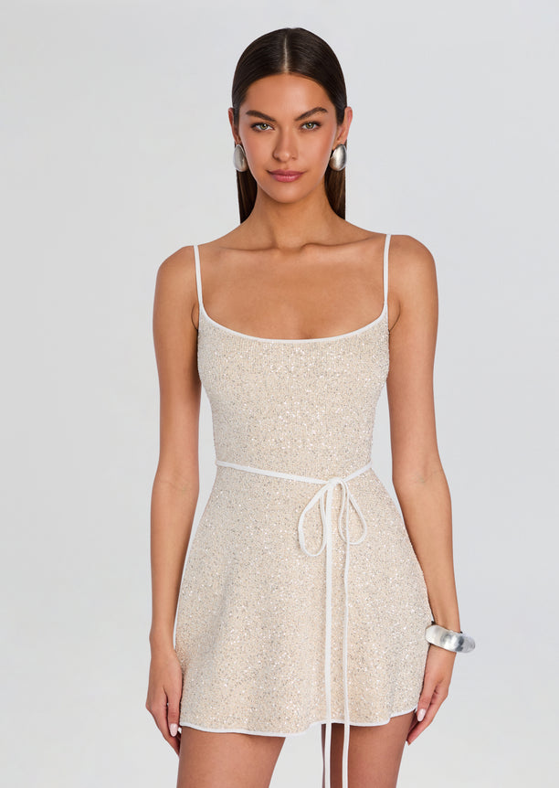 Gisele Dress on a model wearing champagne sequin mini dress with thin straps and a white belt, styled with silver earrings and bracelet.