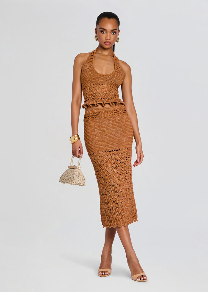 Front view of a model wearing the Leony Crochet Skirt two piece set in tan, featuring a halter top and matching lace crochet midi skirt, with a woven handbag. media 2 of 5