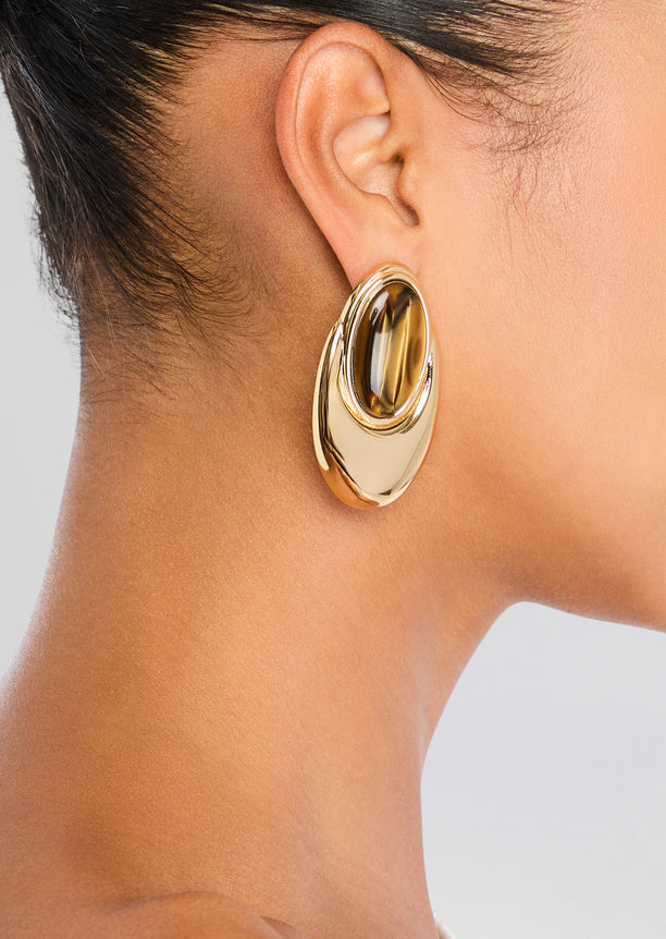 Closeup of Blare Earring on ear featuring a gold oval hoop with a dark tortoiseshell centerpiece.