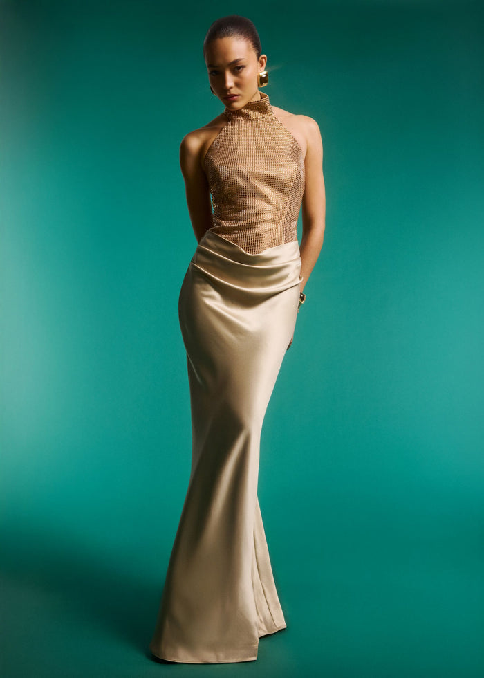 Full-length gold embellished halter dress with a glittering mesh bodice and satin skirt against a teal backdrop. media 2 of 6