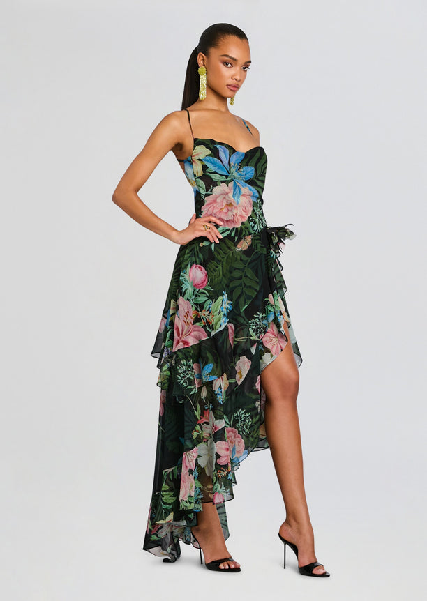 Full-length side view of a model in the Samara Silk Chiffon Dress with a high low floral skirt and black heeled sandals.