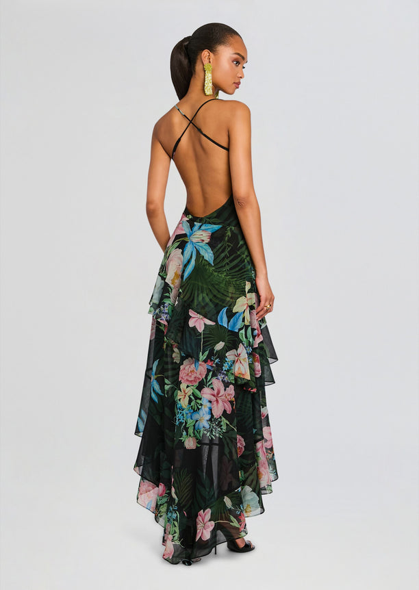 Back view of a model in a tropical floral silk chiffon dress with crisscross back straps and layered sheer ruffles.