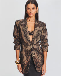Model wearing a taupe lace blazer with bold black floral pattern over a black bralette.