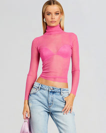 Piper Top worn as a sheer pink knit turtleneck with a visible bra, paired with light wash jeans.