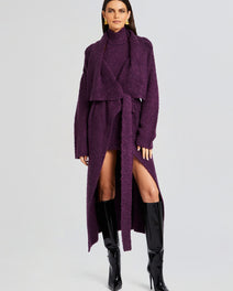 Model wearing a purple Rue Cardigan belted over a matching knit set with knee high patent boots