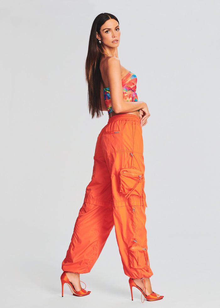 Model wearing a colorful strapless tropical tie-dye tube top with bright orange cargo pants and orange high-heeled sandals. media 3 of 5