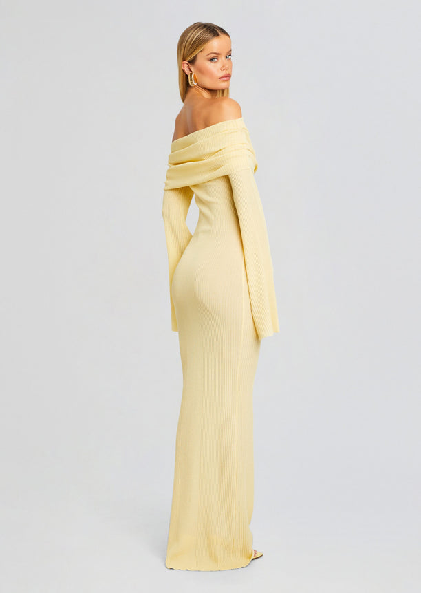 Side profile of a model wearing a pale yellow off-the-shoulder ribbed maxi dress.