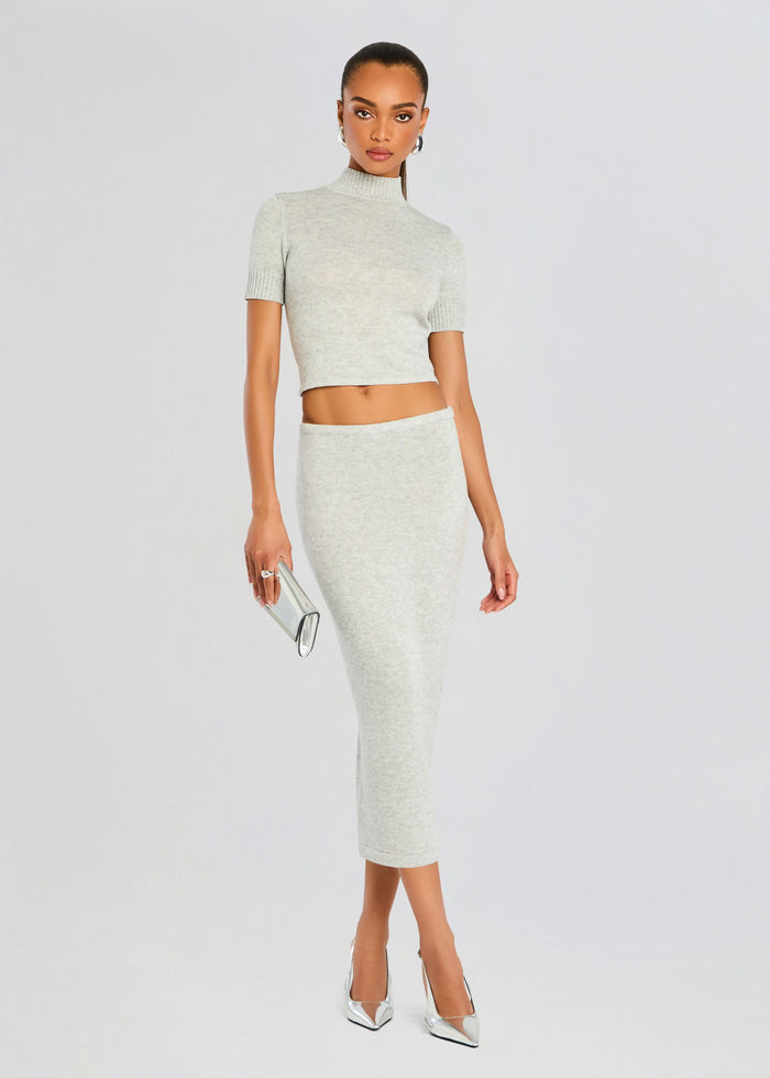 Model in a matching light grey Kali Knit set, cropped top with short sleeves and high waist midi skirt, holding a metallic silver clutch. media 2 of 6