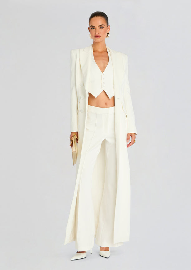 Front view of a white Amberly Blazer Evening Dress styled with a cropped vest and wide leg pants, clutch in hand.