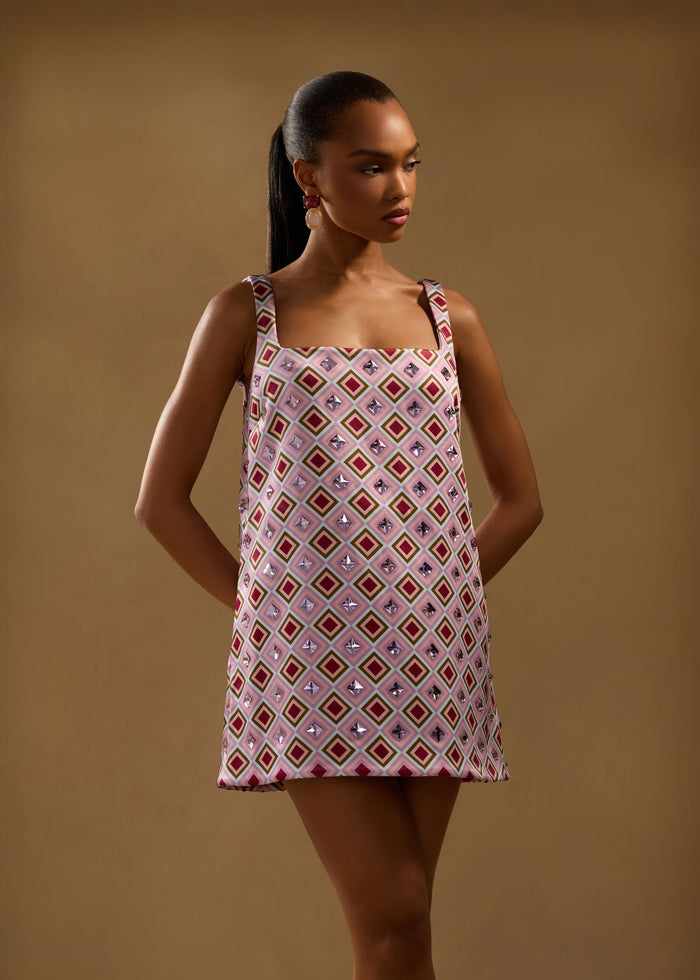 Full-length view of a model wearing the Zephyra Embellished Dress in a pink geometric print with crystal accents. media 2 of 6