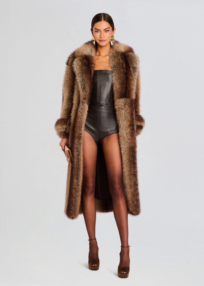 Full-length shot of a model in a brown faux fur coat over a black leather bodysuit against a light backdrop. media 1 of 7