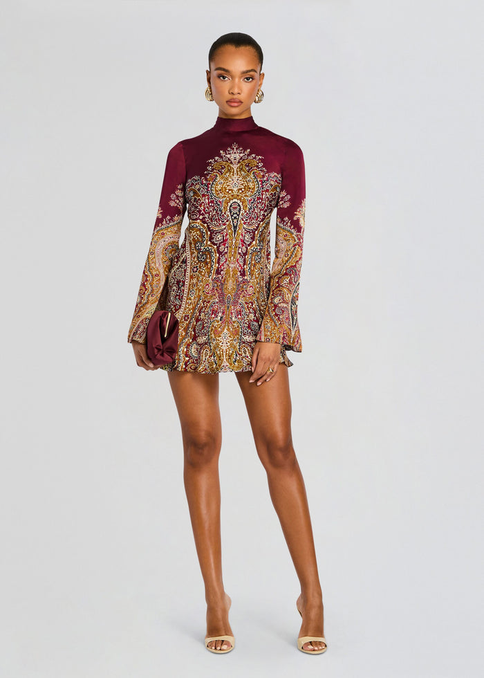 Shifa Mini Dress on a model in burgundy and gold paisley print with long sleeves and a burgundy clutch media 5 of 5