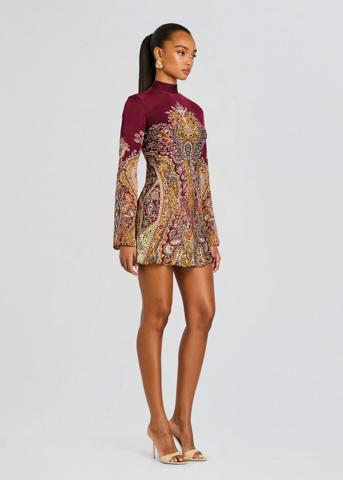 Model wearing burgundy high neck paisley mini dress with long sleeves and beige heeled sandals. media 3 of 5