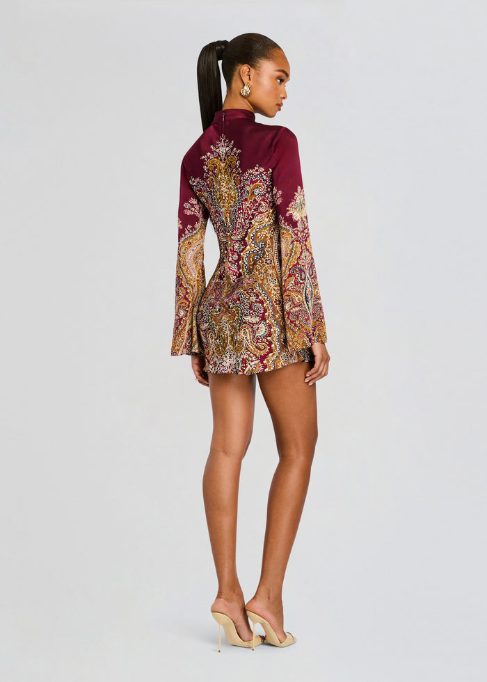 Back view of model in burgundy paisley mini dress with long sleeves, holding a burgundy clutch. media 4 of 5