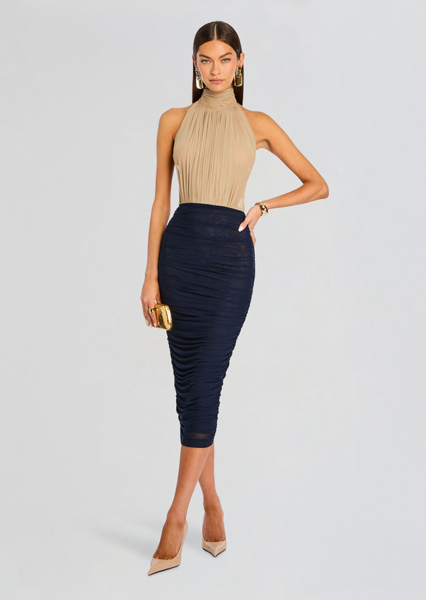 Full length view of a model wearing a beige pleated halter neck bodysuit with a navy ruched midi skirt and nude heels