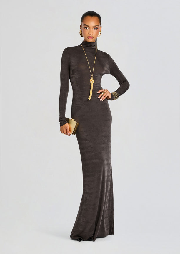 Model in a charcoal turtleneck maxi dress poses with a gold clutch and statement jewelry.