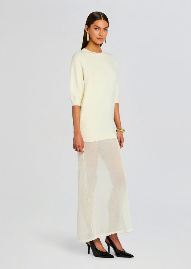 Side view of a model in the Arwen Knit Maxi Dress cream knit top paired with a sheer ankle length skirt