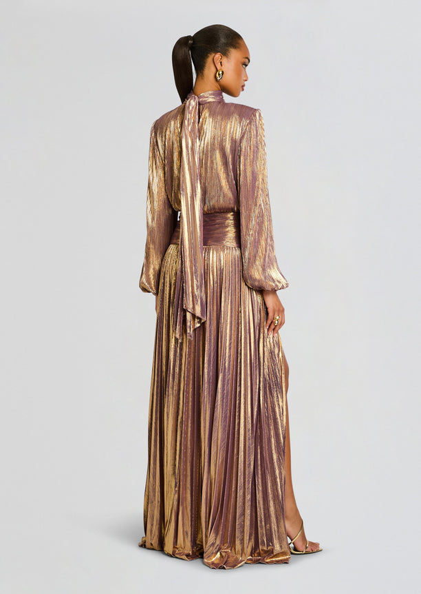 Back view of Brienne Dress in metallic rose and gold pleated fabric with a neck tie and waist sash and a side slit