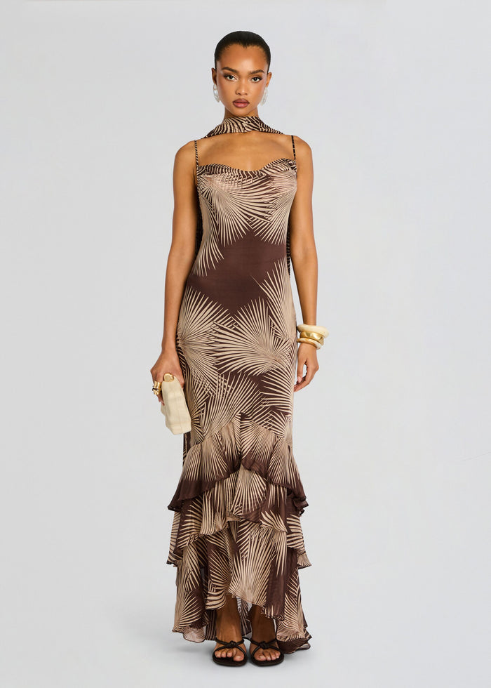 Front full-length view of a model in the brown palm print Taro Maxi Dress with a scarf neck and tiered ruffle hem. media 3 of 5