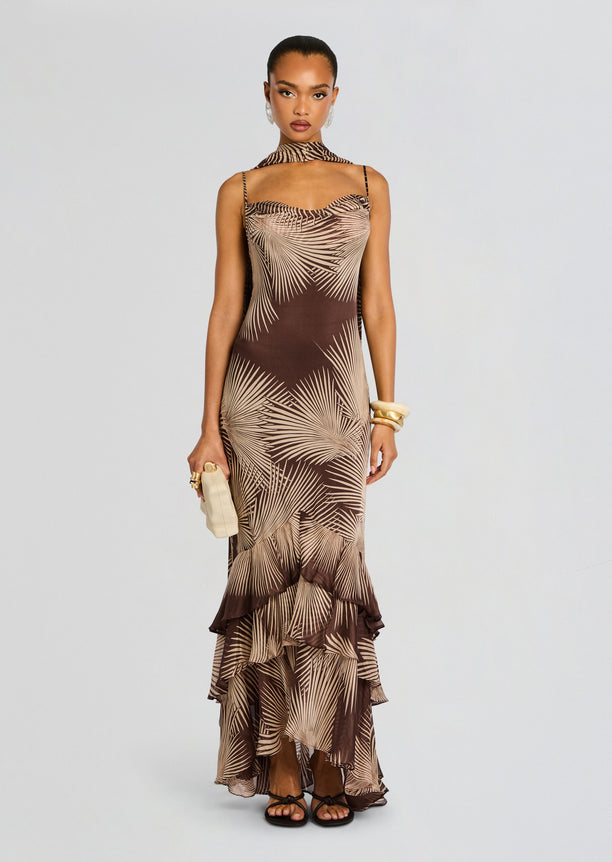 Front full-length view of a model in the brown palm print Taro Maxi Dress with a scarf neck and tiered ruffle hem.