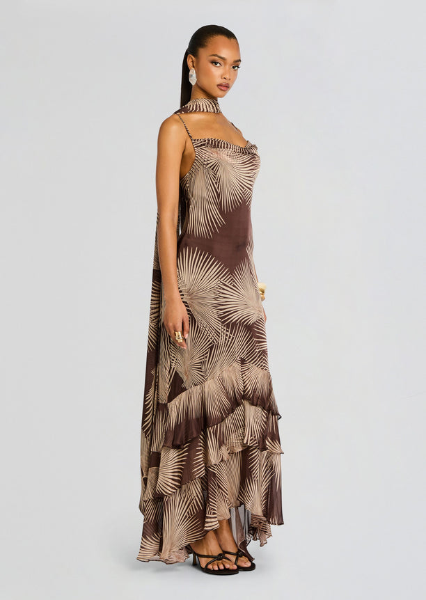 Model wearing brown palm leaf print maxi dress with a matching neck scarf and a layered ruffled hem