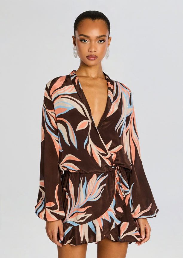 Model wearing Fern Front Wrap Mini Dress featuring brown leaf print, plunging V neckline, wrap front, tied waist, and a short ruffled hem.