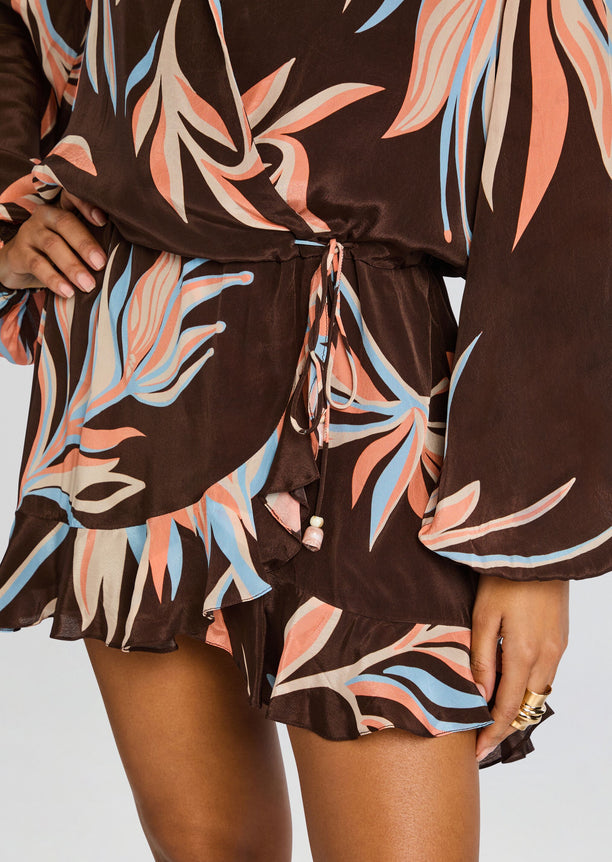 Close-up of the brown tropical print wrap dress showing belt tie and ruffled hem.