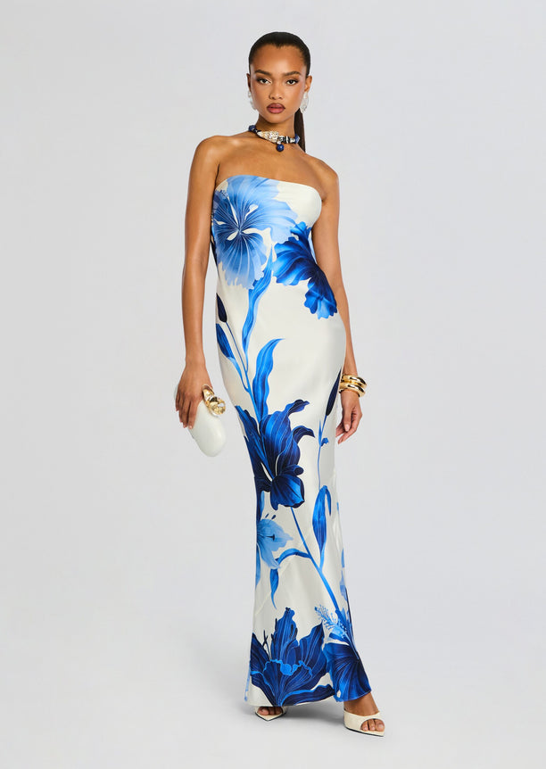 Front view of a model in a strapless blue and white floral silk gown, holding a white clutch and wearing gold bracelets.