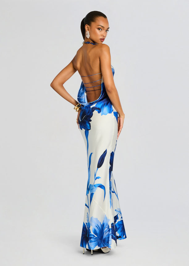 Model wearing a blue and white floral silk dress from the back with a halter neckline and multiple thin back straps.