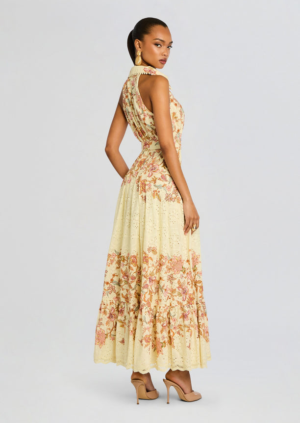 Cream maxi dress with intricate pink floral embroidery and eyelet hem, model in profile.